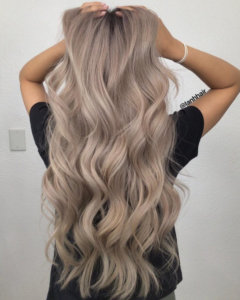 Long ash blonde waves cascade down the back of a person in a black shirt
