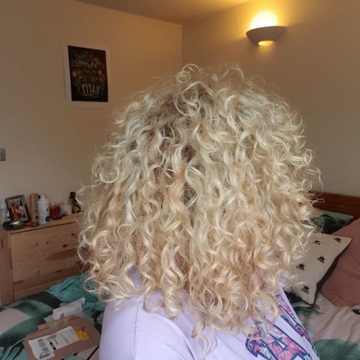 Blonde curly hair falls in voluminous ringlets over a person’s shoulders
