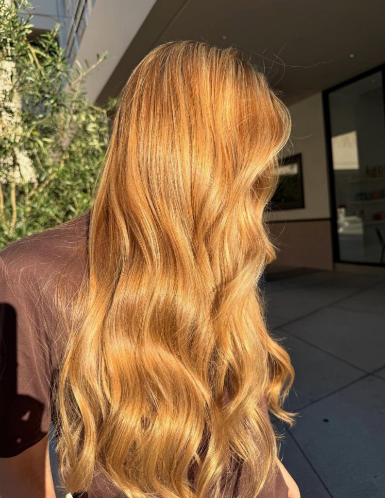 Long wavy golden-blonde hair shining in sunlight outside a modern building