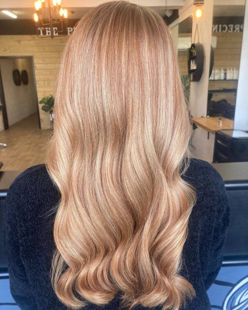 Long strawberry blonde hair with soft waves viewed from behind in a salon