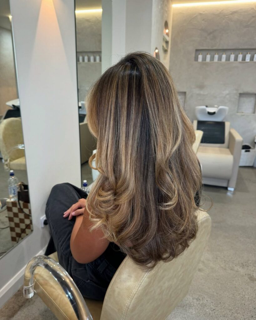 Wavy brown hair with delicate blonde babylights in a salon chair