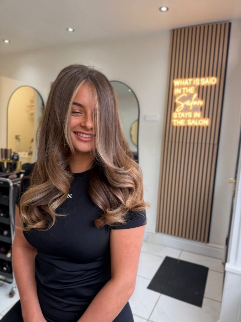 Woman showing long caramel blonde curls with darker roots in a salon
