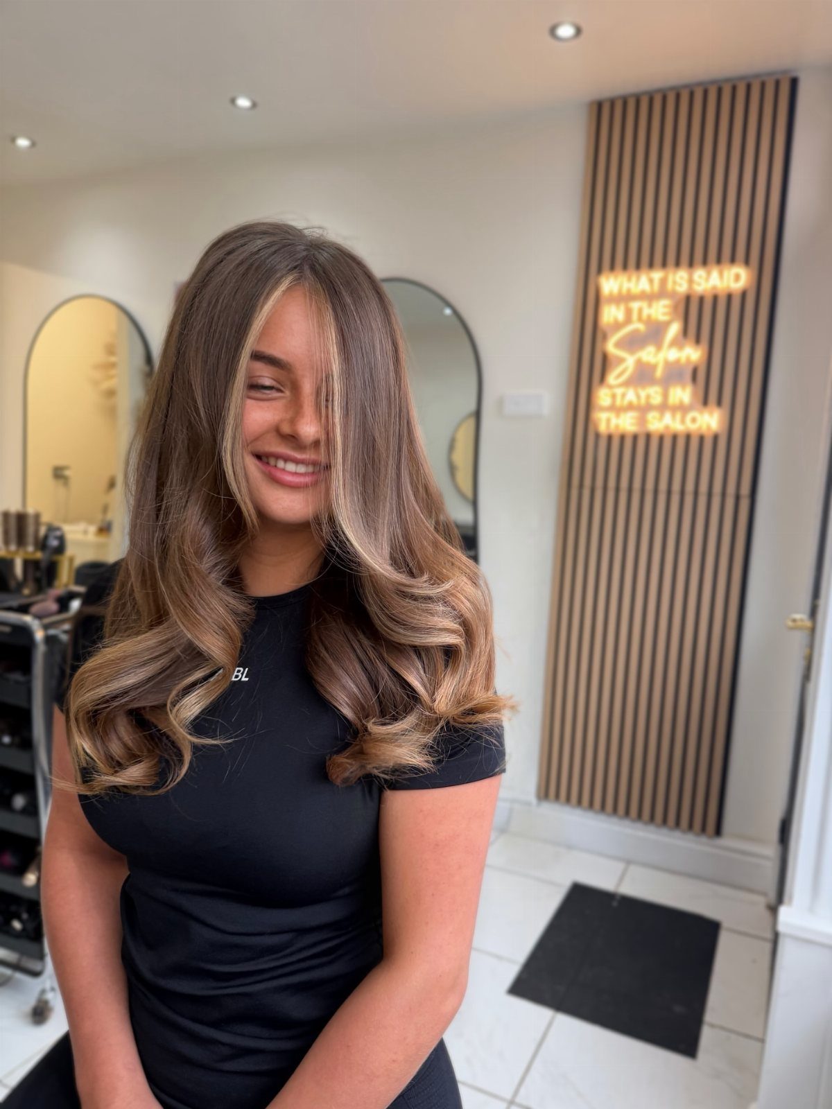 Woman showing long caramel blonde curls with darker roots in a salon