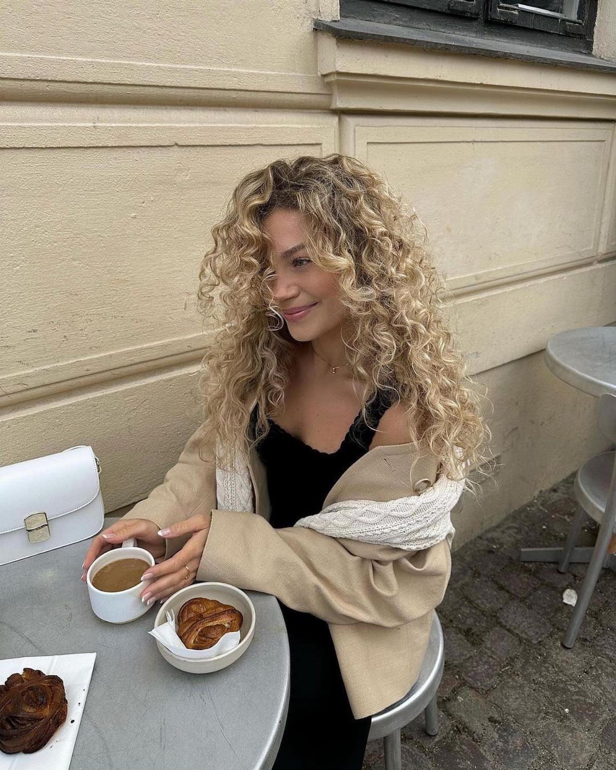 Woman with long blonde curls seated at an outdoor café table