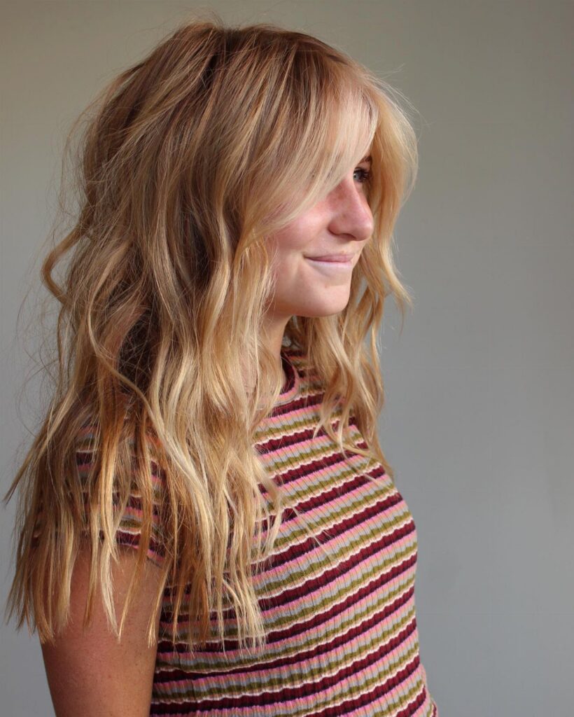Young woman showing long, wavy strawberry blonde hair with side-swept bangs