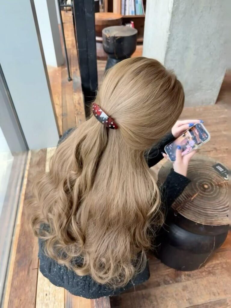 Long golden blonde hair falls in waves beneath a red patterned hair clip