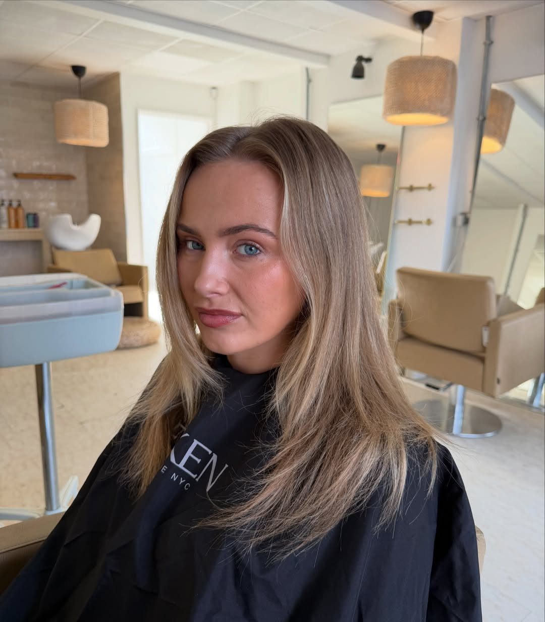 Woman with long honey-blonde hair seated in a bright hair salon