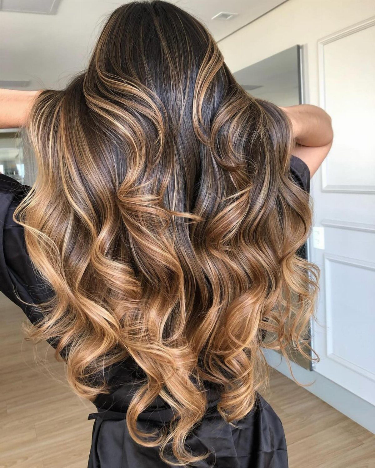 Curled hair transitions from dark brown roots to warm honey-brown ends