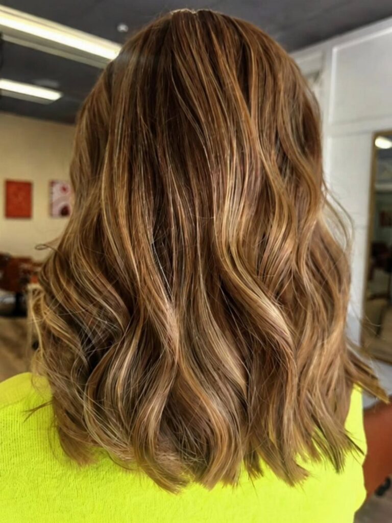 Wavy brunette hair with honey highlights shown from behind in a salon