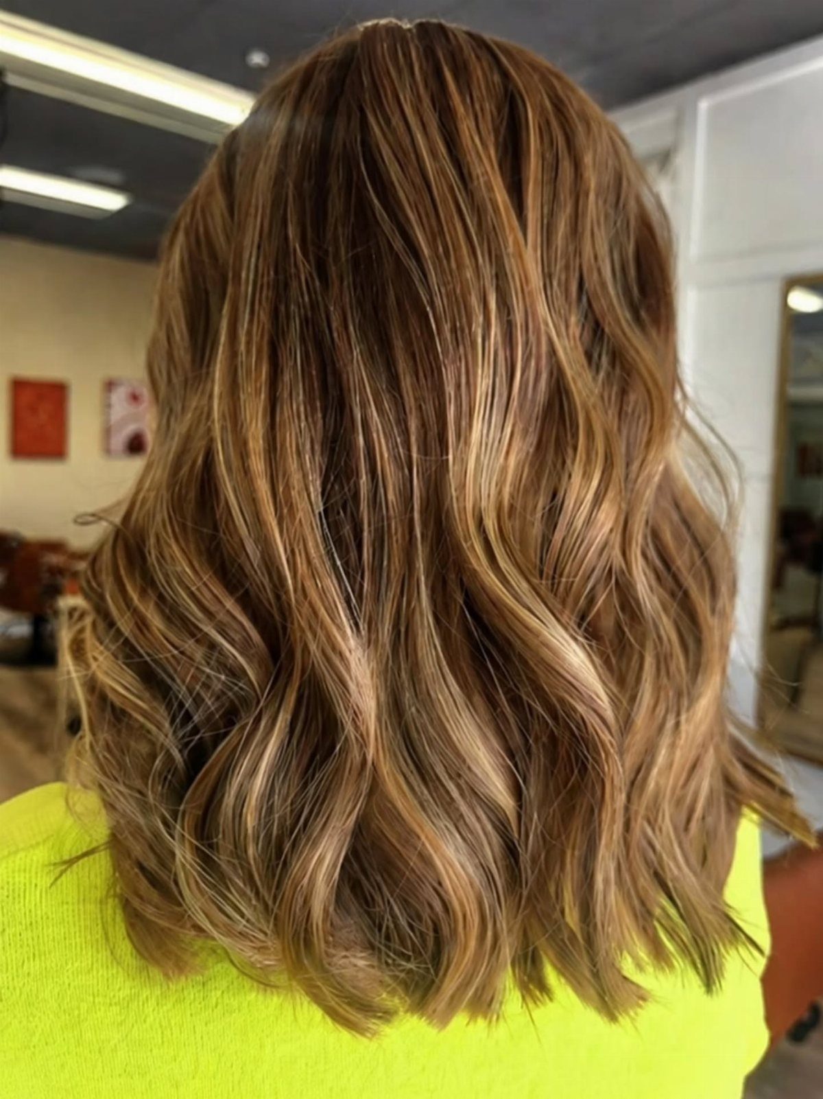 Wavy brunette hair with honey highlights shown from behind in a salon