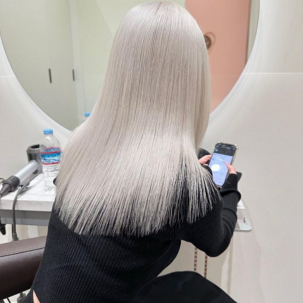 Long, straight ice-blonde hair falls over a black sweater in a salon