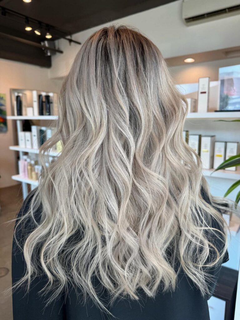 Wavy icy blonde hair with dark roots cascading down a salon client's back