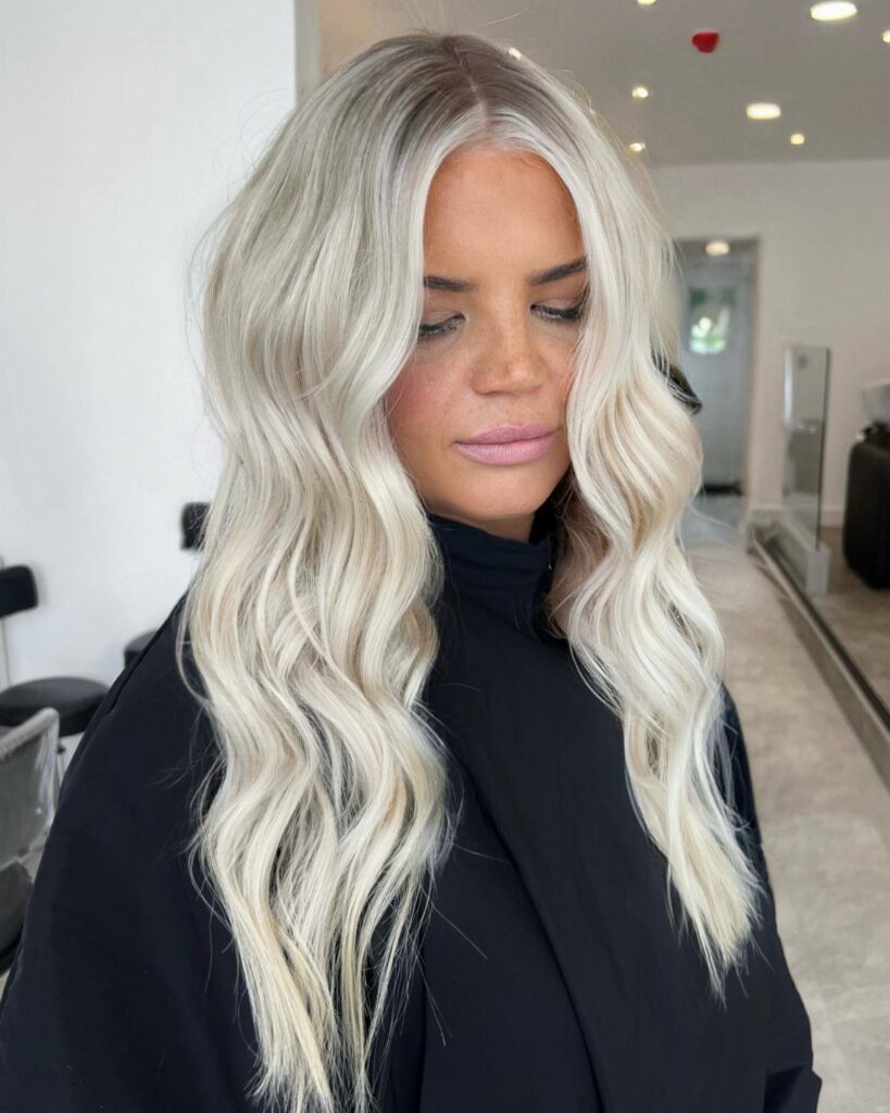 Woman with long wavy icy blonde hair and subtly darker roots in a salon