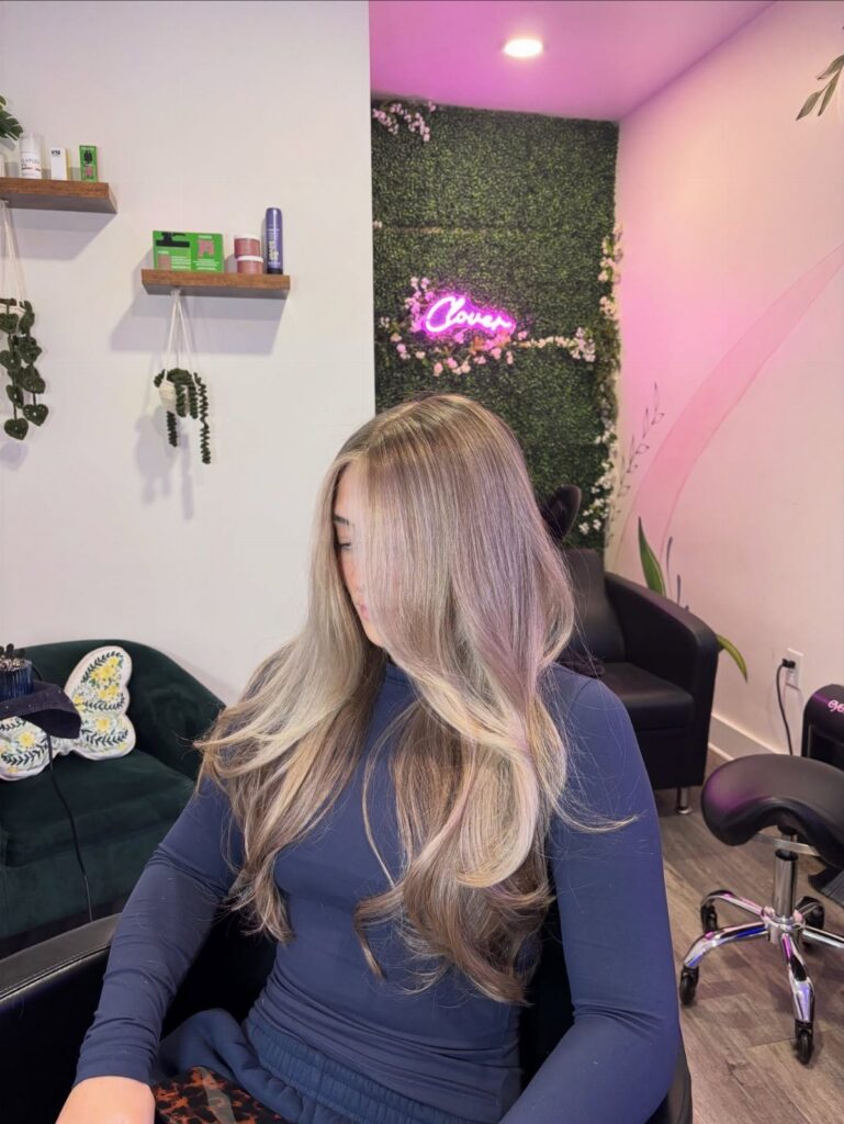 Long blonde layered hair with darker roots styled on a seated salon client