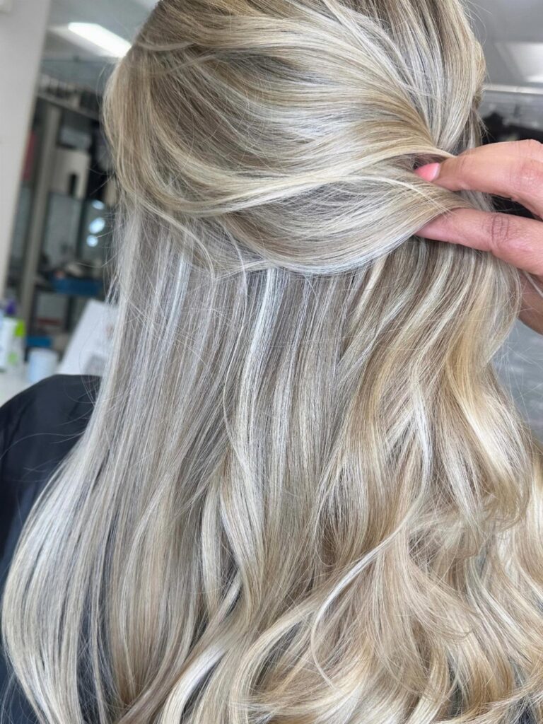 Long ash-blonde hair with darker roots and pale highlights, loosely gathered in a salon