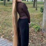 Woman with very long straight blonde hair standing in a leafy park