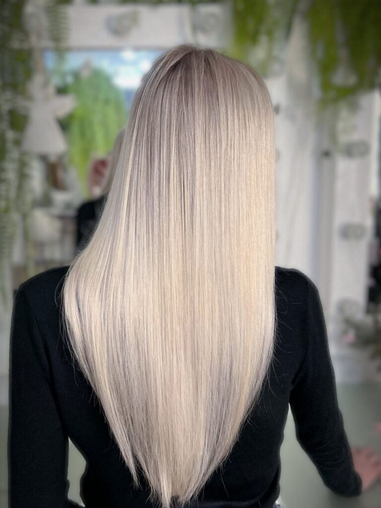 Long, pin-straight platinum blonde hair falls down the back over a black top