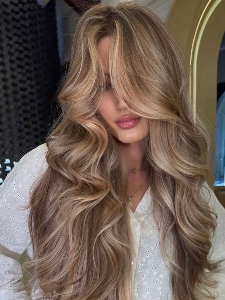 Woman with long, wavy sand-blonde hair wearing a white eyelet blouse