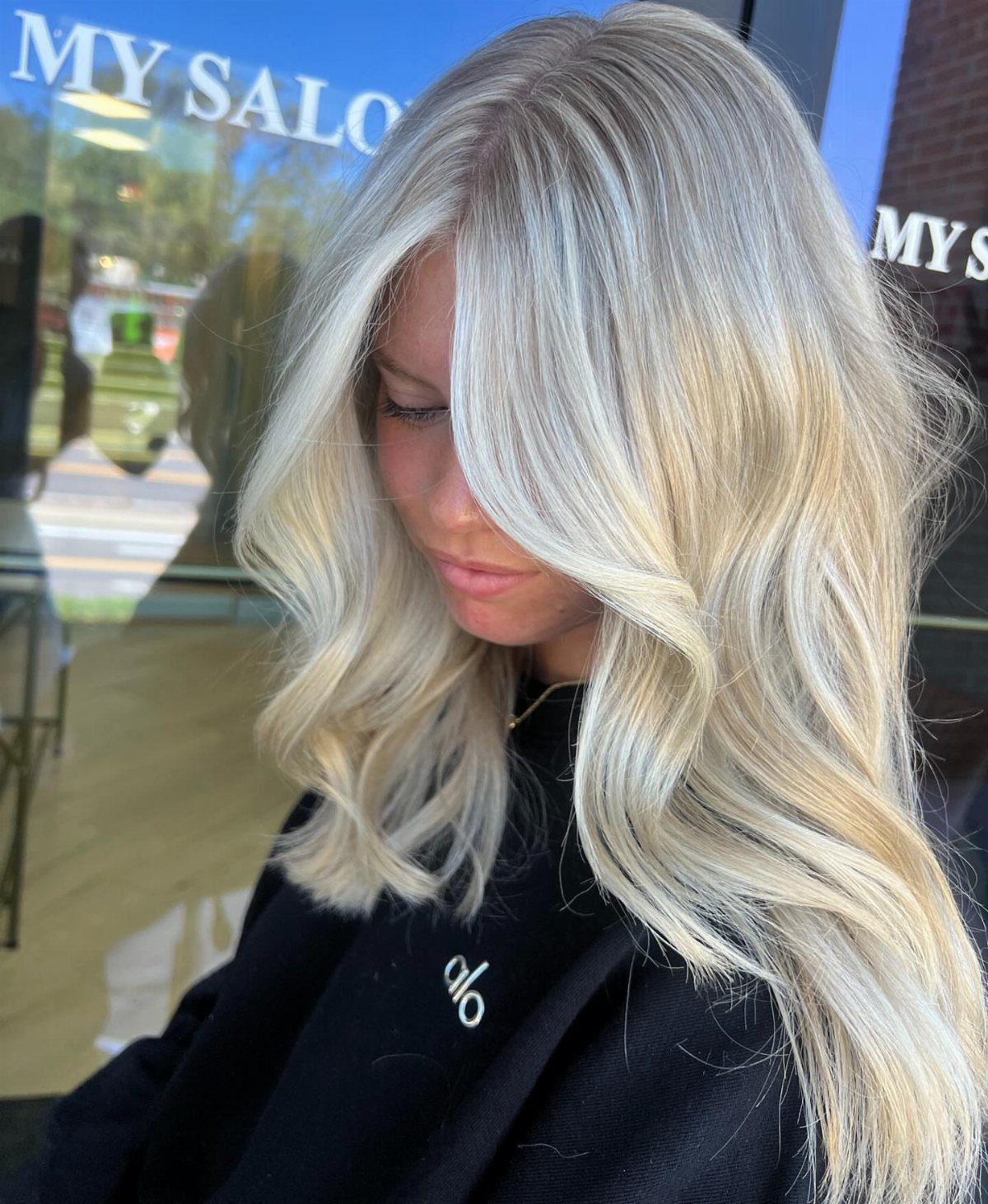 Woman displaying long, wavy white-blonde hair outside a salon